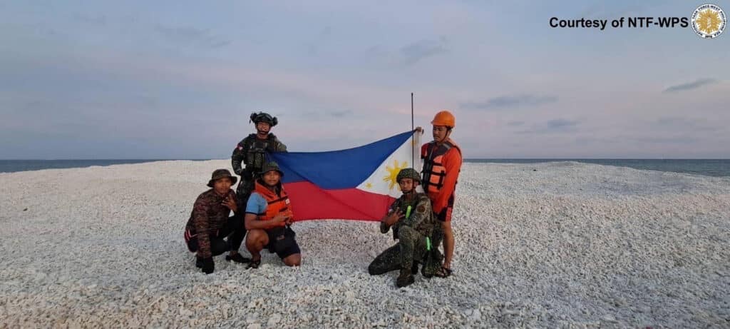 Philippine coast guard and military personnel holding a Philippine flag